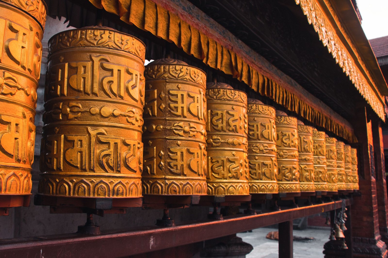 Ornate golden prayer wheels lined up in Kathmandu, Nepal, showcasing rich cultural heritage and Buddhism.