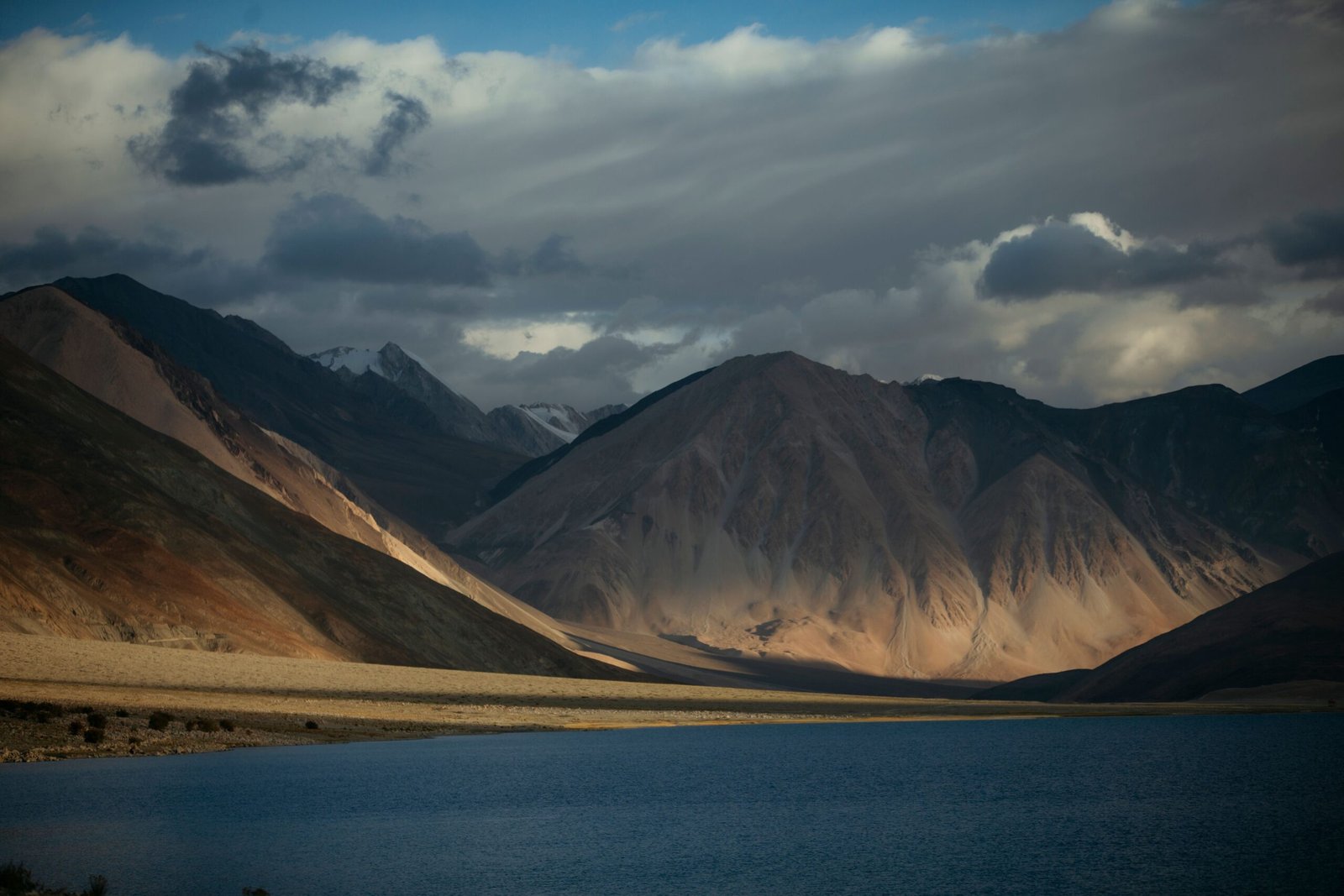Breathtaking view of Pangong Lake with mountains and dynamic clouds in Ladakh, India.