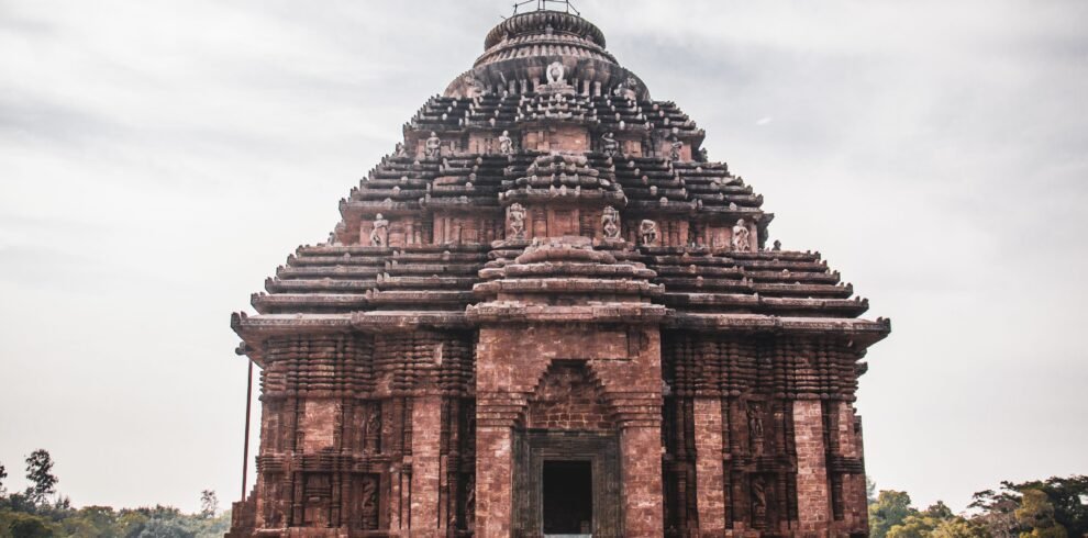 Exterior of main building of historical Hindu Konark Sun Temple with carved details and sculptures on roof against cloudy sky