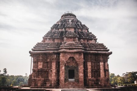 Exterior of main building of historical Hindu Konark Sun Temple with carved details and sculptures on roof against cloudy sky